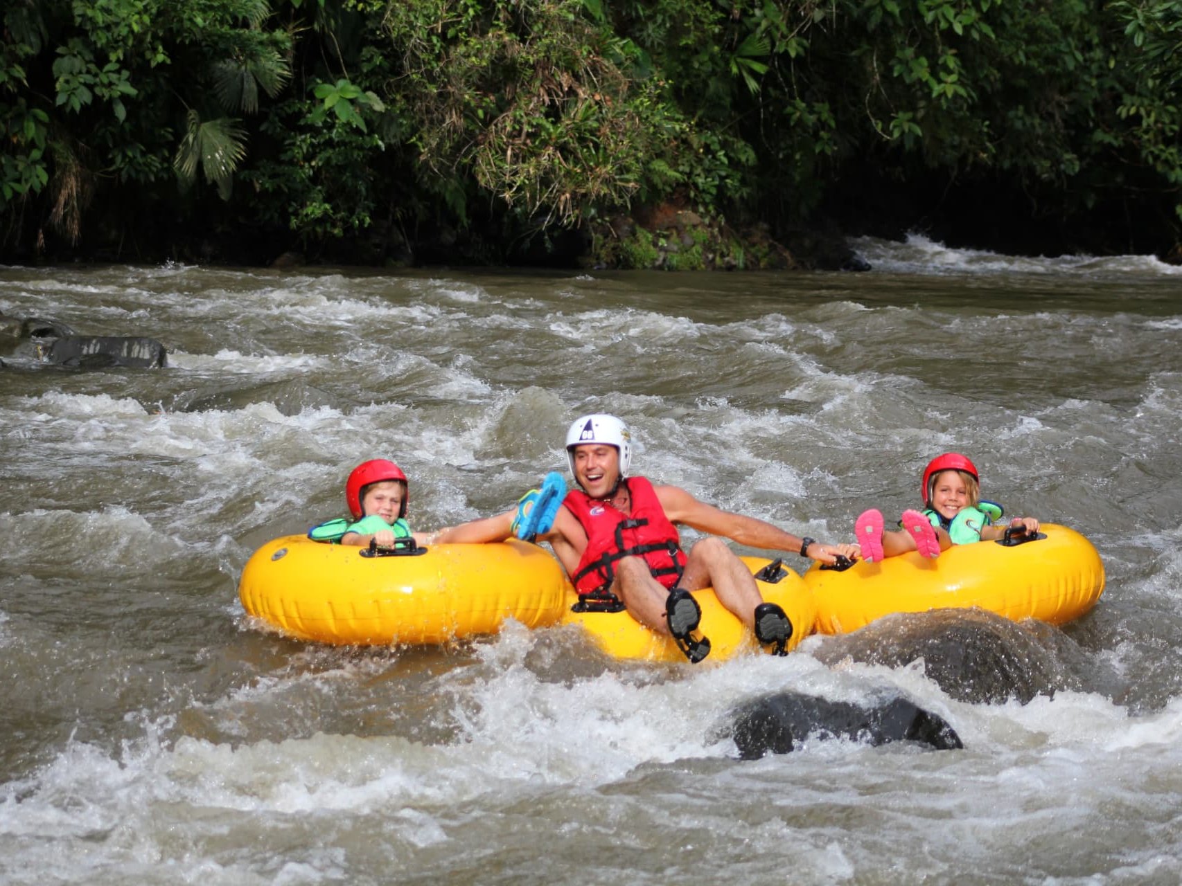 A parent and two children river tubing through the rainforest